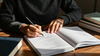 Pessoa concentrada estudando em uma mesa iluminada por luz natural, rodeada de livros, caderno e caneta, transmitindo motivação e foco