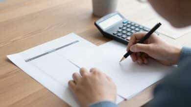 Pessoa analisando planilhas e calculadora, reorganizando as finanças pessoais com determinação em um ambiente organizado