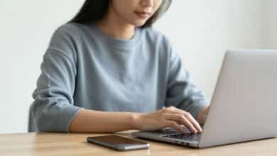 Pessoa concentrada usando notebook com celular desligado ao lado, ambiente limpo e silencioso.