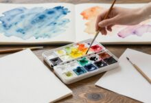 Imagem de capa mostrando uma paleta de aquarela, pincéis e papéis brancos prontos para pintura