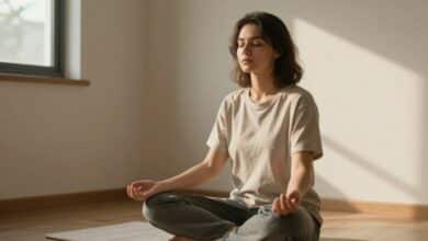Uma pessoa serena sentada em uma posição confortável com os olhos fechados, praticando uma técnica de respiração em um ambiente calmo e iluminado pela luz natural.