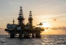 Uma imponente plataforma de petróleo no meio do oceano durante o nascer do sol, com um helicóptero se aproximando para pouso, ilustrando o dinâmico ambiente das profissões para trabalhar embarcado.