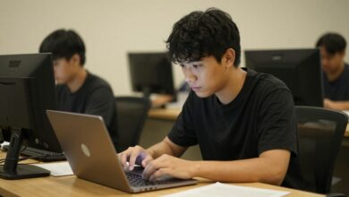 Uma pessoa trabalhando concentrada em um laptop com o celular virado para baixo ao lado, em um ambiente de trabalho calmo e organizado.